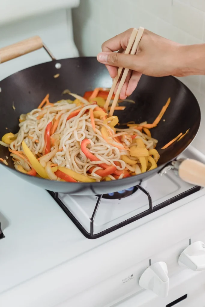 Noodles and peppers being stir fried in a wok with chopsticks on a home hob