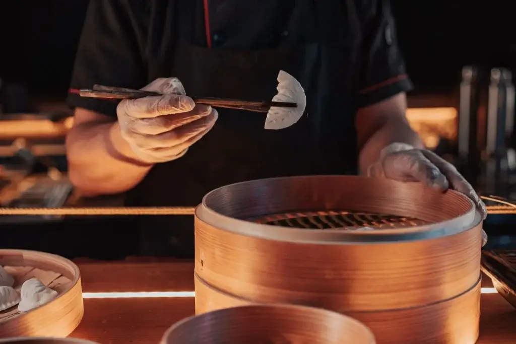Cook placing dumplings into a bamboo steamer with chopsticks