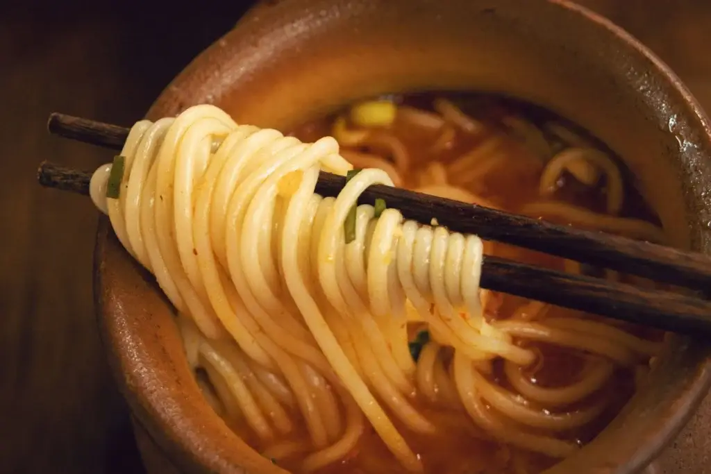 Bowl of spicy Asian noodles lifted with chopsticks