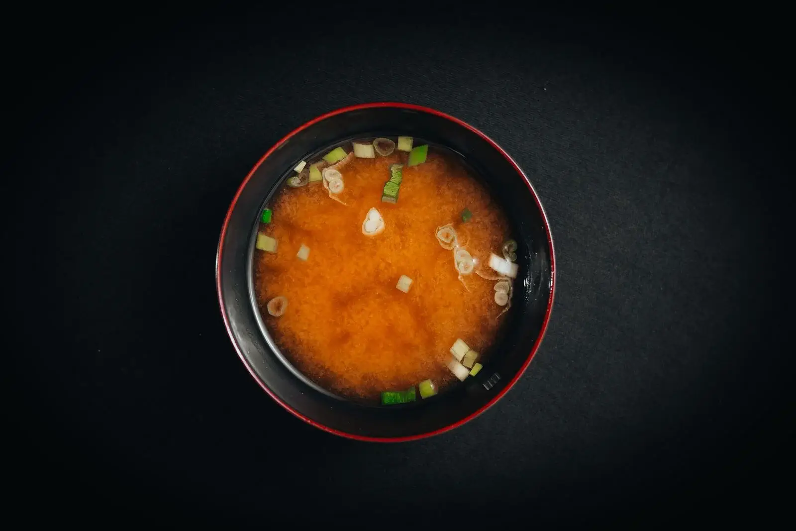 Miso soup with spring onion and tofu in a black bowl