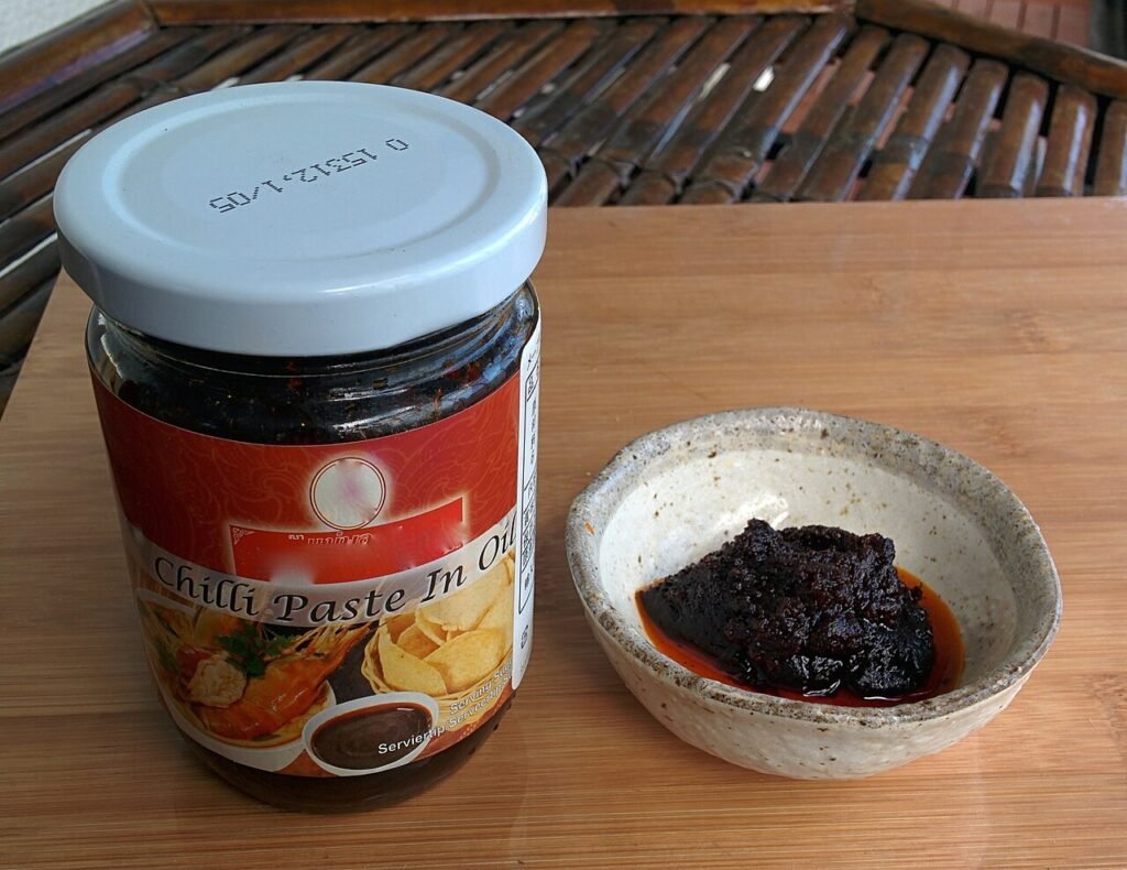 Jar of Thai chilli paste in oil next to a small bowl of it
