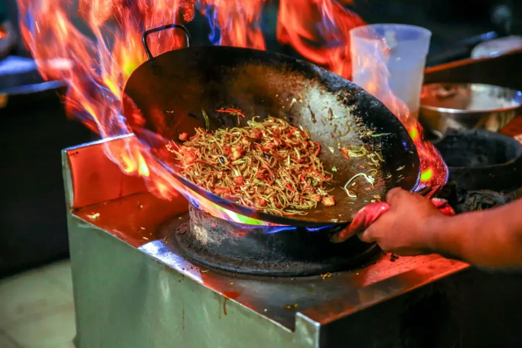 Chef cooking noodles in a flaming wok